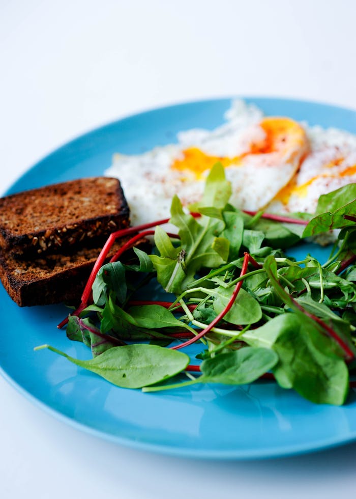 why-choose-us Close-up of a nutritious breakfast with eggs, green salad, and toast on a blue plate.