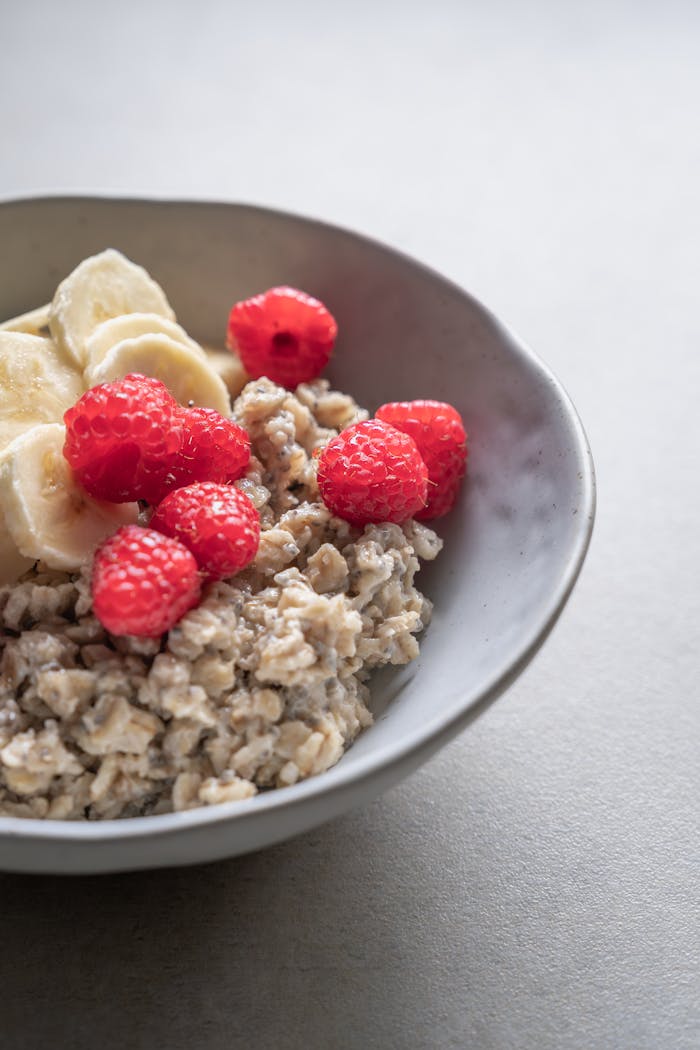 Healthy oatmeal topped with fresh banana slices and raspberries in a bowl.
