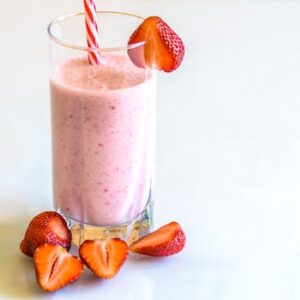 Delicious strawberry smoothie in a glass with fresh strawberries and a striped straw on a light background.