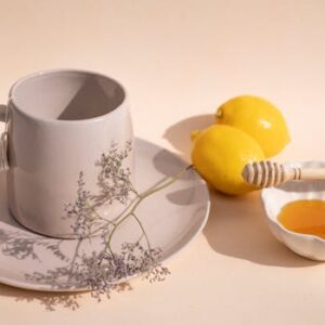 Aesthetic arrangement of a ceramic cup, lemons, and honey dipper for tea preparation.