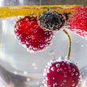 Close-up of fresh berries and lemon slice in sparkling water with bubbles.