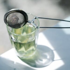 A tea strainer resting on a glass with sunlight casting shadows, creating a serene tea-making ambiance.