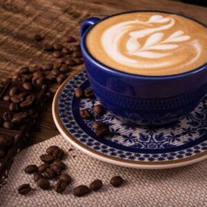 Artistic cappuccino in a blue cup with coffee beans and chocolate on rustic wooden surface.